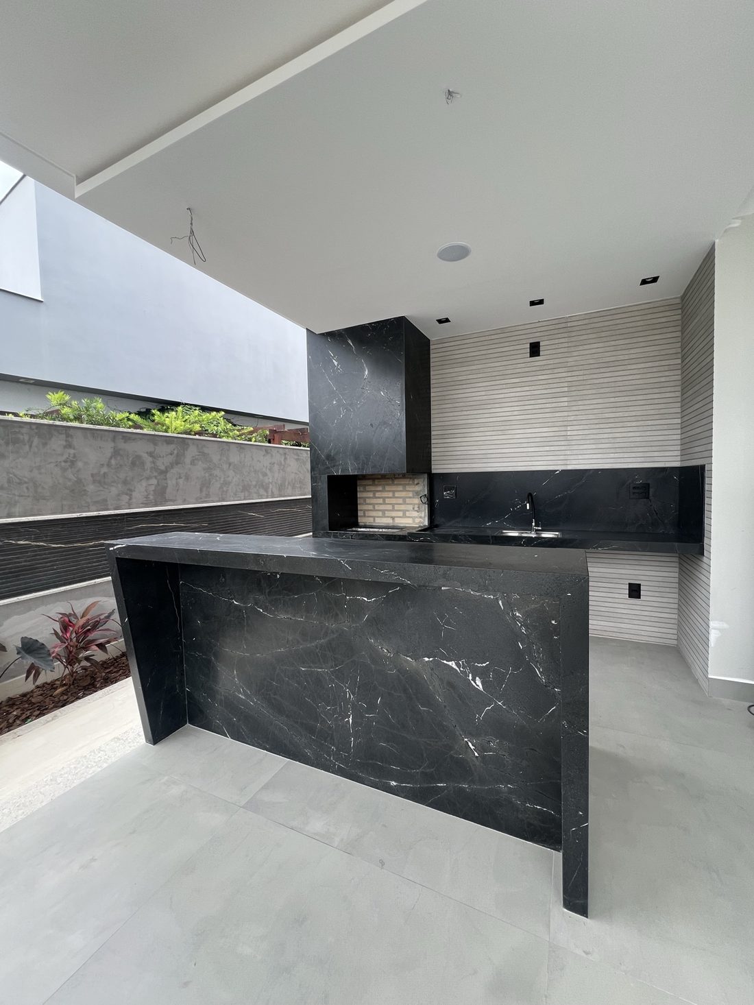 Espaço gourmet com bancada e churrasqueira revestidas em pedra grafite com veios brancos