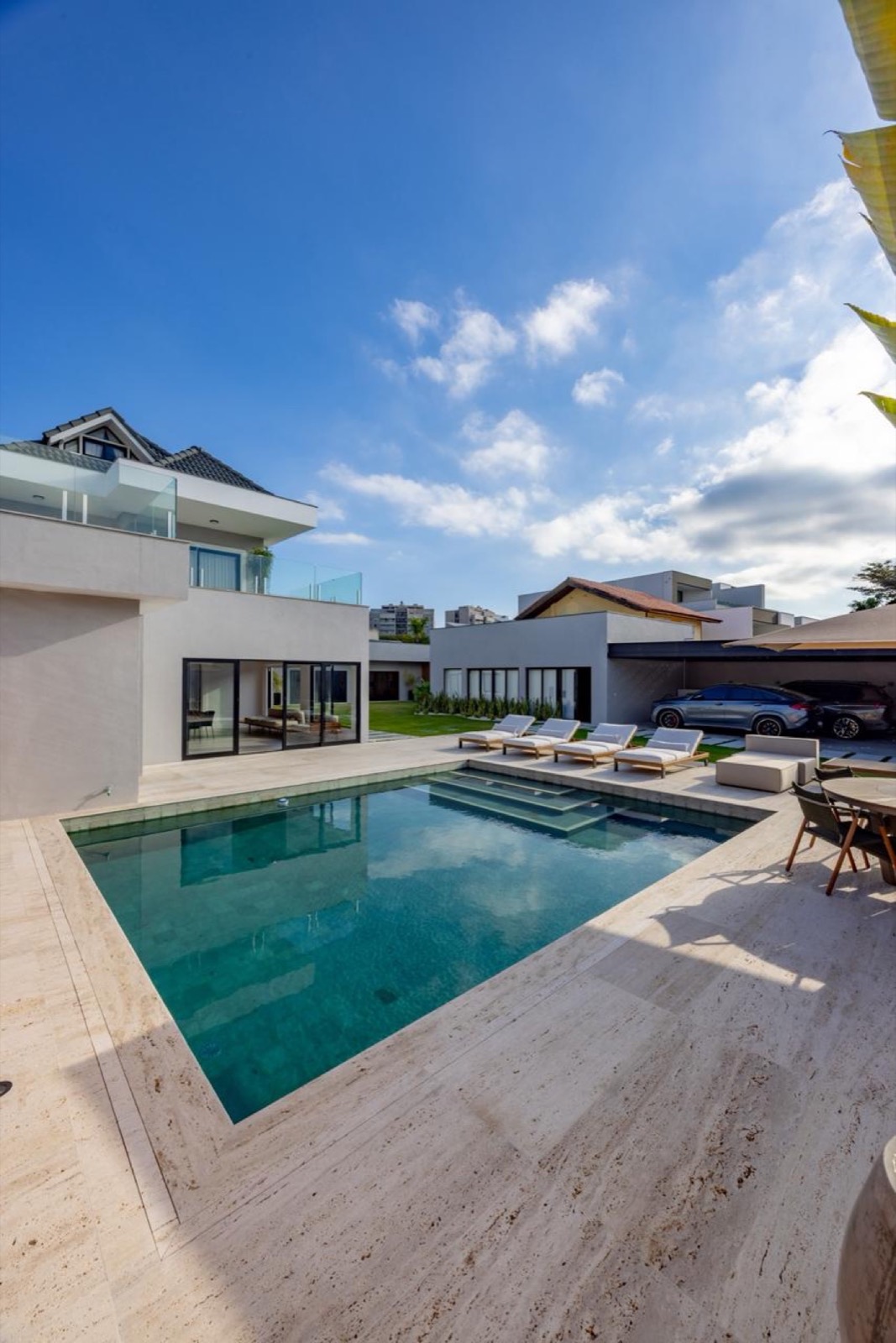 Piscina retangular com entorno em travertino claro e casa branca